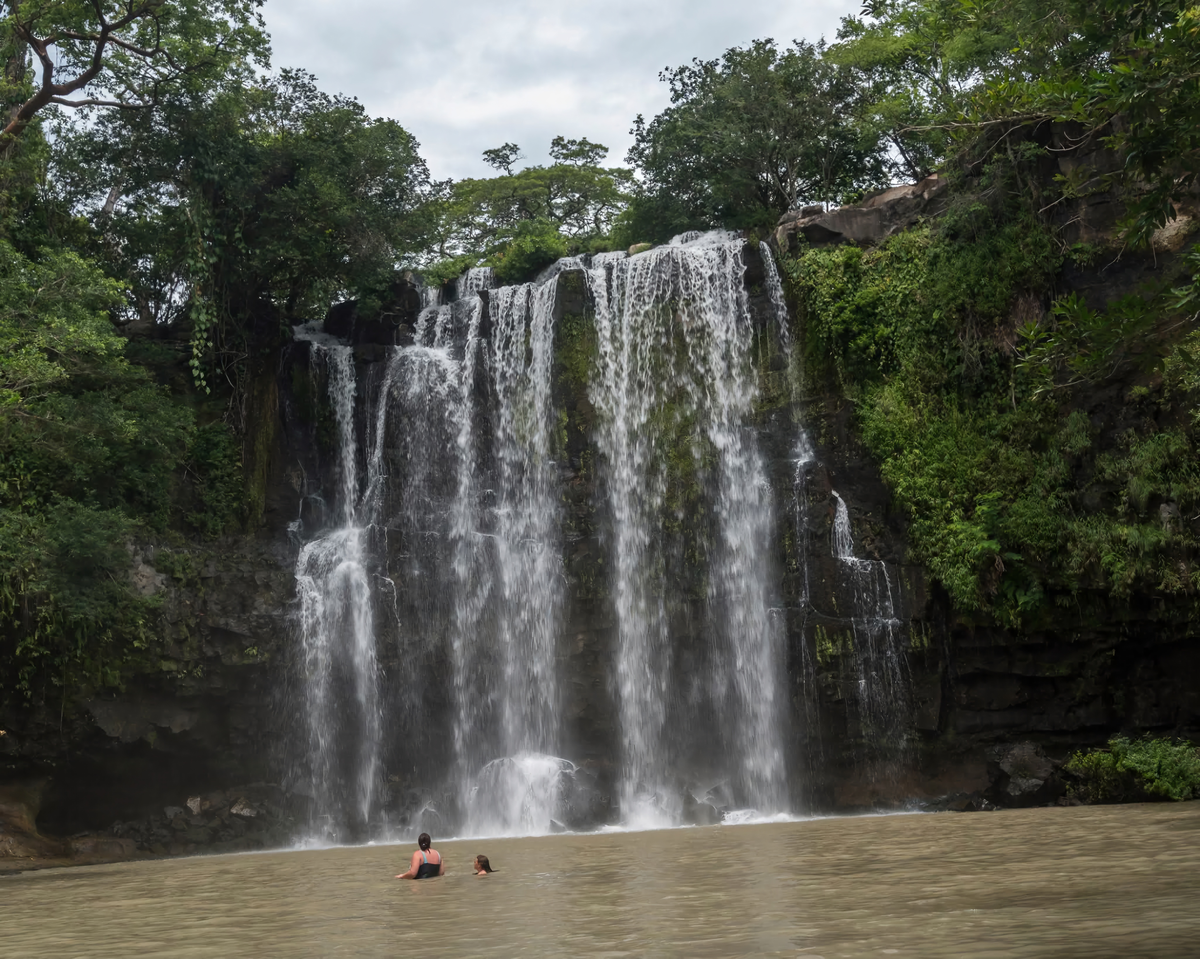 Visitors swimming at Llanos de Cortés Waterfall in Costa Rica, surrounded by lush greenery and cascading jungle falls